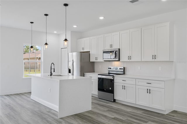 kitchen with sink, hanging light fixtures, an island with sink, white cabinetry, and stainless steel appliances