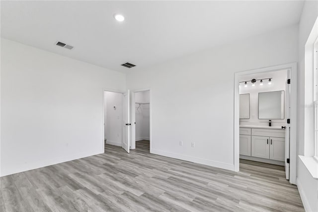 unfurnished bedroom featuring a walk in closet, sink, connected bathroom, light hardwood / wood-style floors, and a closet