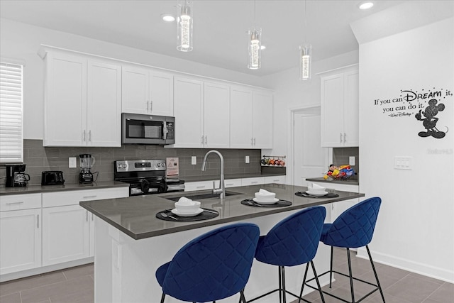 kitchen featuring a kitchen island with sink, sink, appliances with stainless steel finishes, decorative light fixtures, and white cabinetry