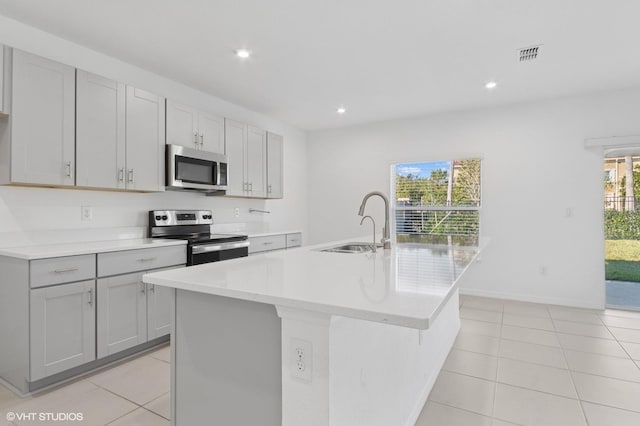 kitchen with gray cabinetry, sink, stainless steel appliances, a center island with sink, and light tile patterned floors