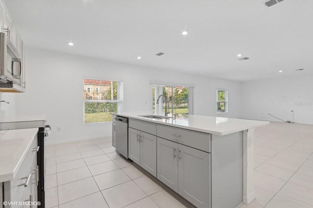 kitchen with appliances with stainless steel finishes, sink, a center island with sink, gray cabinets, and light tile patterned flooring