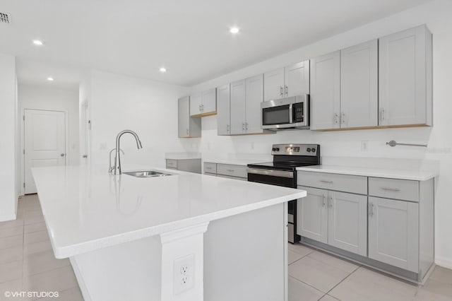 kitchen featuring a kitchen island with sink, sink, gray cabinets, light tile patterned floors, and stainless steel appliances