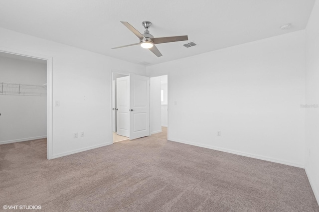 unfurnished bedroom with ceiling fan, a walk in closet, light carpet, and a closet