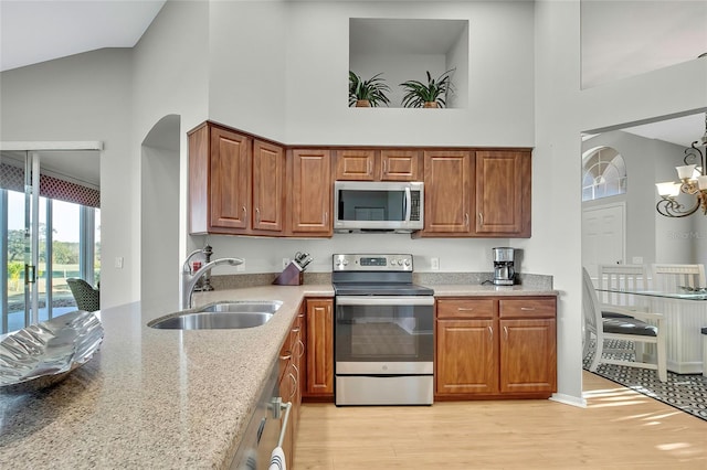 kitchen with high vaulted ceiling, sink, light hardwood / wood-style flooring, stainless steel appliances, and a chandelier