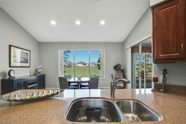 kitchen featuring light stone counters, lofted ceiling, sink, and a wealth of natural light