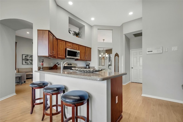 kitchen with an inviting chandelier, a towering ceiling, light hardwood / wood-style floors, a kitchen bar, and stainless steel appliances