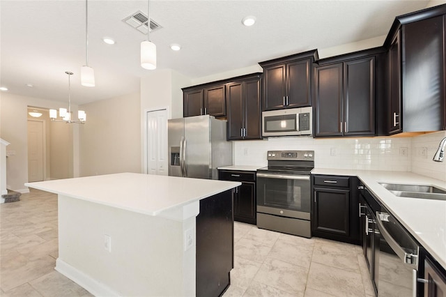 kitchen with appliances with stainless steel finishes, backsplash, sink, a kitchen island, and hanging light fixtures