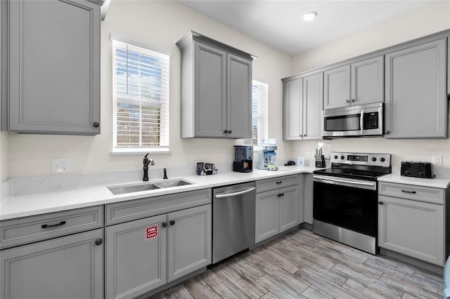 kitchen featuring gray cabinetry, sink, light hardwood / wood-style flooring, light stone counters, and stainless steel appliances