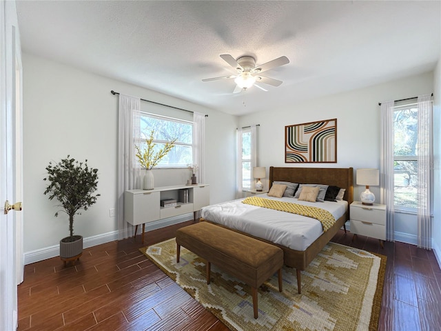 bedroom with multiple windows, ceiling fan, dark wood-type flooring, and a textured ceiling