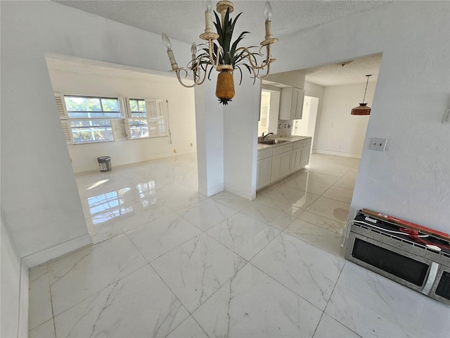 kitchen featuring white cabinets, a textured ceiling, an inviting chandelier, and sink