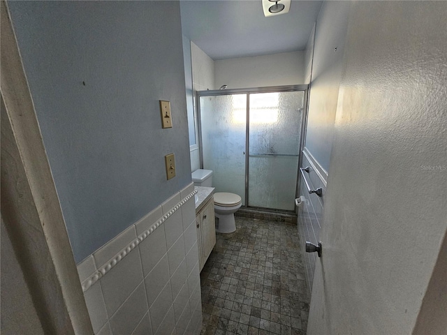 bathroom featuring tile patterned floors, vanity, tile walls, toilet, and a shower with shower door