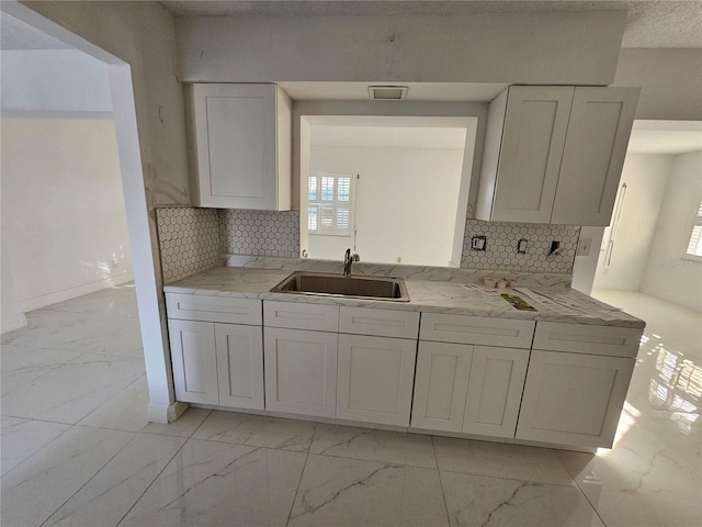 kitchen with light stone countertops, backsplash, a healthy amount of sunlight, sink, and white cabinets