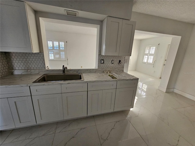 kitchen with tasteful backsplash, white cabinetry, sink, and a textured ceiling