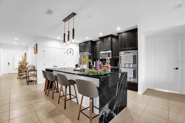 1651 Kingfisher Ct, Kissimmee, FL 34746 - kitchen featuring stainless steel appliances, a center island with sink, light tile patterned floors, a kitchen breakfast bar, and dark cabinets
