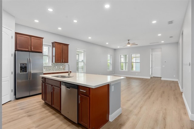 kitchen featuring light wood-type flooring, stainless steel appliances, ceiling fan, sink, and an island with sink