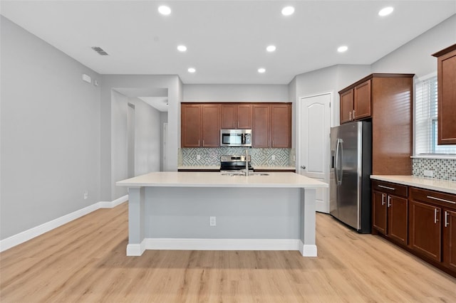 kitchen with tasteful backsplash, a center island with sink, light wood-type flooring, and appliances with stainless steel finishes