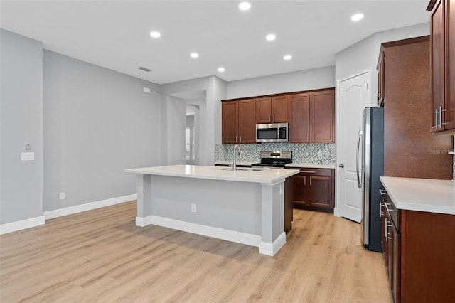 kitchen with a center island with sink, sink, decorative backsplash, appliances with stainless steel finishes, and light hardwood / wood-style floors