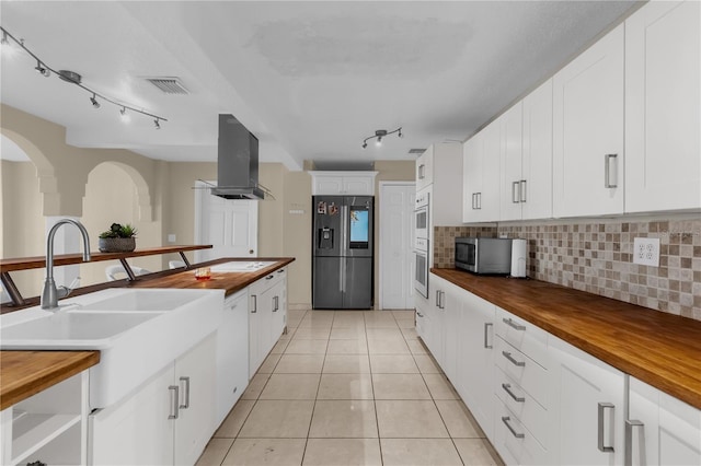 kitchen with white cabinetry, tasteful backsplash, wooden counters, island range hood, and appliances with stainless steel finishes