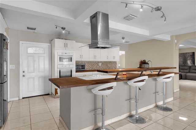 kitchen with appliances with stainless steel finishes, light tile patterned floors, white cabinetry, and range hood