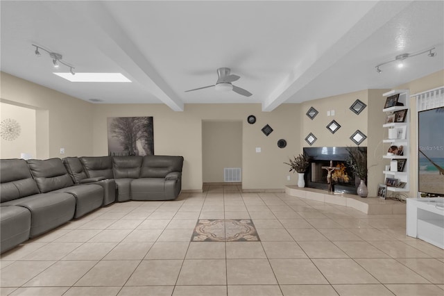 living room with track lighting, ceiling fan, light tile patterned floors, a fireplace, and beam ceiling