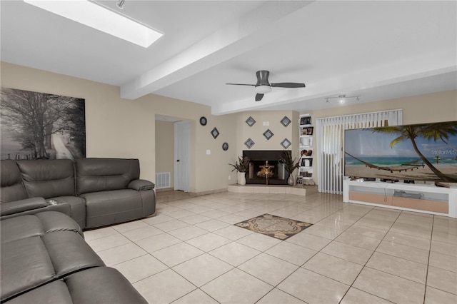 living room with beam ceiling, ceiling fan, a fireplace, and light tile patterned floors