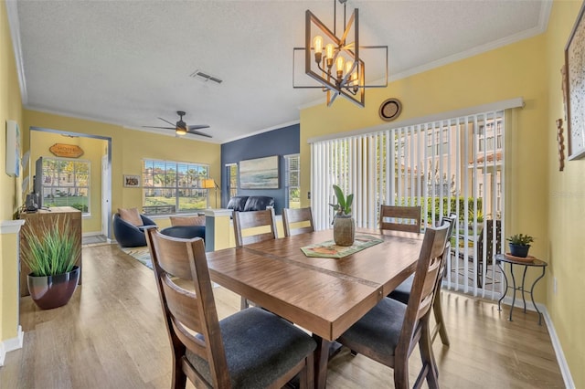 dining space with ceiling fan with notable chandelier, ornamental molding, a textured ceiling, and light wood-type flooring