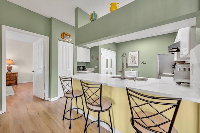 kitchen featuring kitchen peninsula, stainless steel fridge, light hardwood / wood-style floors, a breakfast bar, and white cabinets