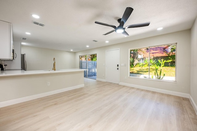 unfurnished living room featuring ceiling fan, a healthy amount of sunlight, light wood-type flooring, and sink