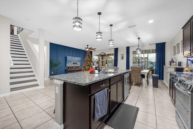 kitchen featuring appliances with stainless steel finishes, dark stone counters, dark brown cabinetry, sink, and an island with sink