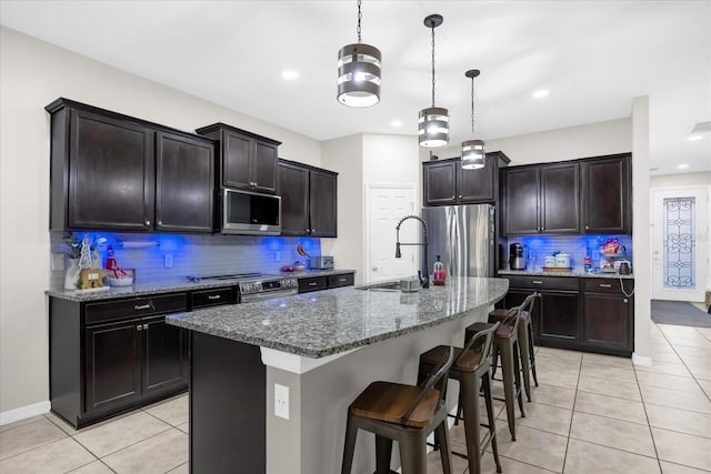 kitchen with appliances with stainless steel finishes, backsplash, sink, decorative light fixtures, and an island with sink