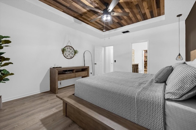 bedroom with hardwood / wood-style floors, wooden ceiling, ensuite bathroom, ceiling fan, and a tray ceiling