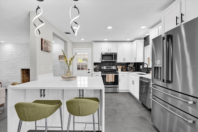 kitchen featuring decorative backsplash, stainless steel appliances, sink, white cabinets, and hanging light fixtures