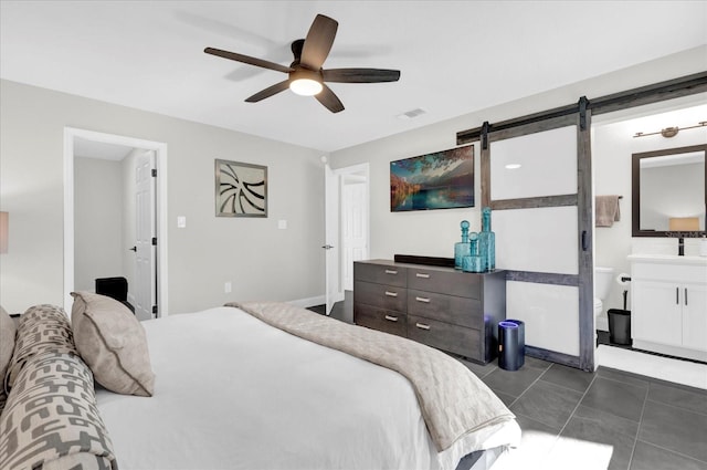 bedroom featuring ensuite bath, ceiling fan, dark tile patterned floors, and a barn door