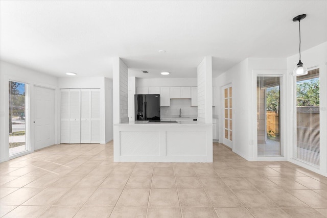 kitchen with pendant lighting, white cabinets, black fridge, and light tile patterned flooring