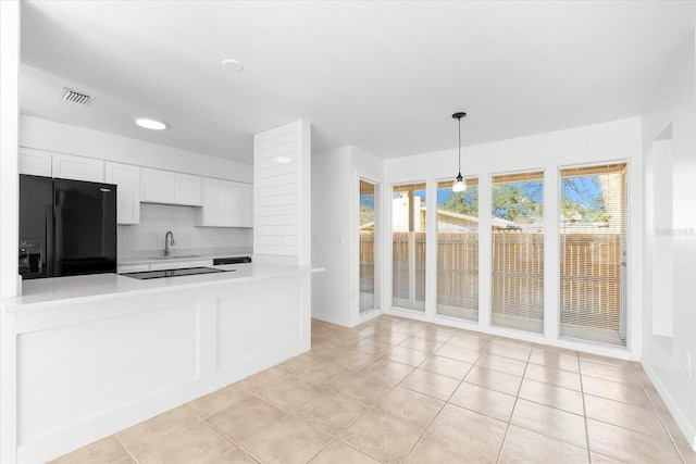 kitchen featuring white cabinetry, kitchen peninsula, decorative backsplash, black fridge, and pendant lighting