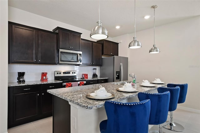 kitchen featuring tasteful backsplash, a center island with sink, pendant lighting, and appliances with stainless steel finishes