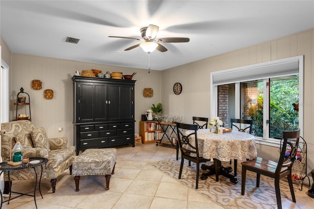 tiled dining space featuring ceiling fan and wooden walls