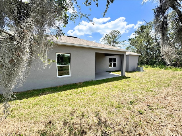 rear view of property with central air condition unit, a patio area, a lawn, and stucco siding