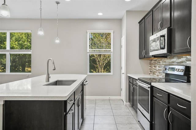 kitchen featuring sink, stainless steel appliances, tasteful backsplash, decorative light fixtures, and a center island with sink