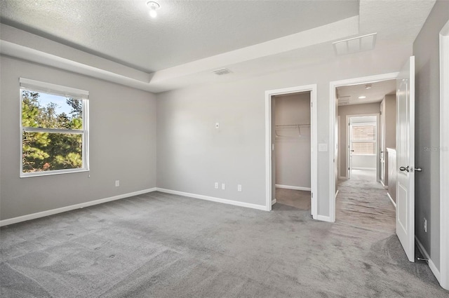 unfurnished bedroom with a closet, a walk in closet, carpet floors, and a textured ceiling