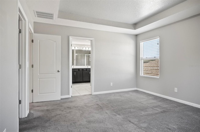 carpeted spare room with a tray ceiling and a textured ceiling