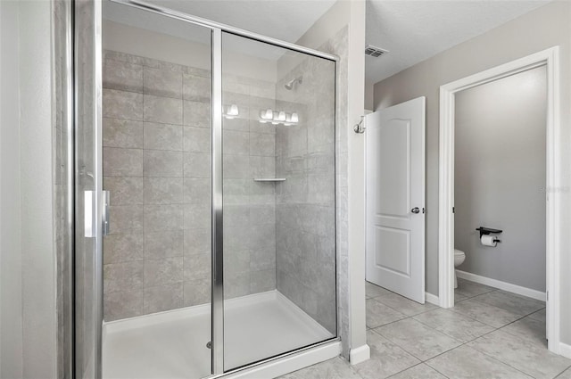 bathroom featuring a shower with shower door, toilet, and tile patterned flooring