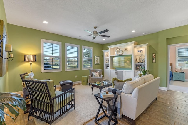 living room featuring ceiling fan, light wood-type flooring, and a textured ceiling