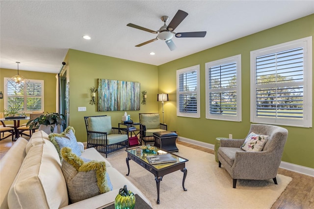 living room featuring wood-type flooring, ceiling fan with notable chandelier, a textured ceiling, and a wealth of natural light