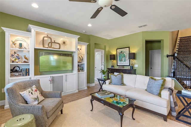 living room with built in shelves, a textured ceiling, light hardwood / wood-style flooring, and ceiling fan