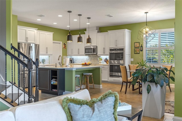 kitchen with pendant lighting, a breakfast bar, white cabinets, a center island with sink, and stainless steel appliances