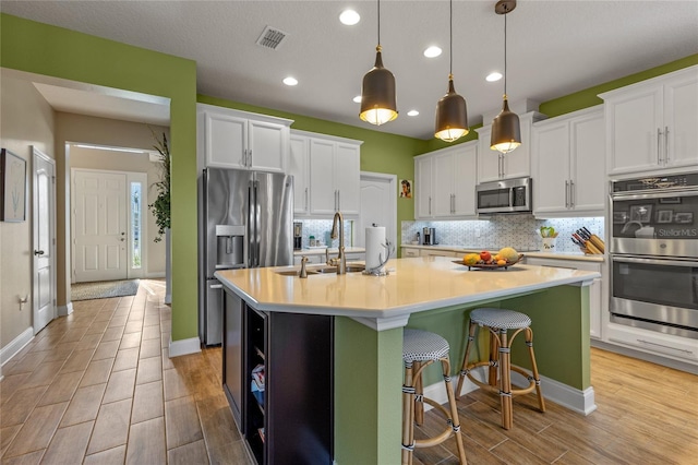 kitchen with white cabinets, a kitchen island with sink, and appliances with stainless steel finishes