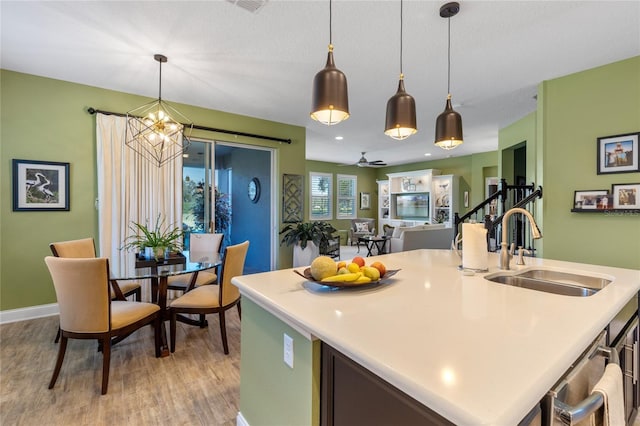 kitchen featuring light wood-type flooring, ceiling fan with notable chandelier, a kitchen island with sink, sink, and pendant lighting