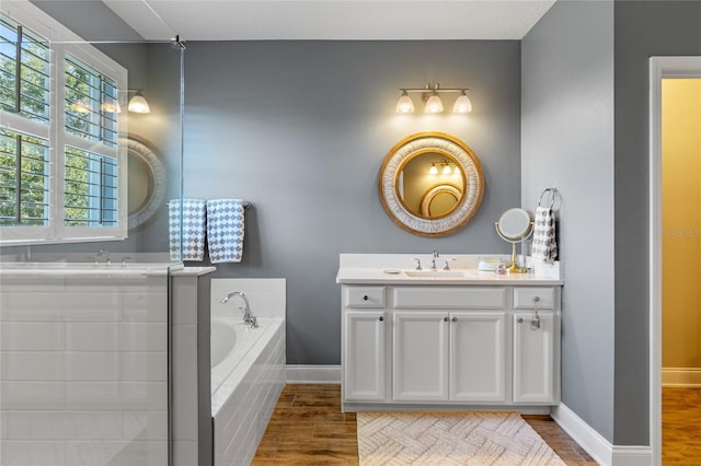 bathroom with hardwood / wood-style flooring, vanity, and tiled tub