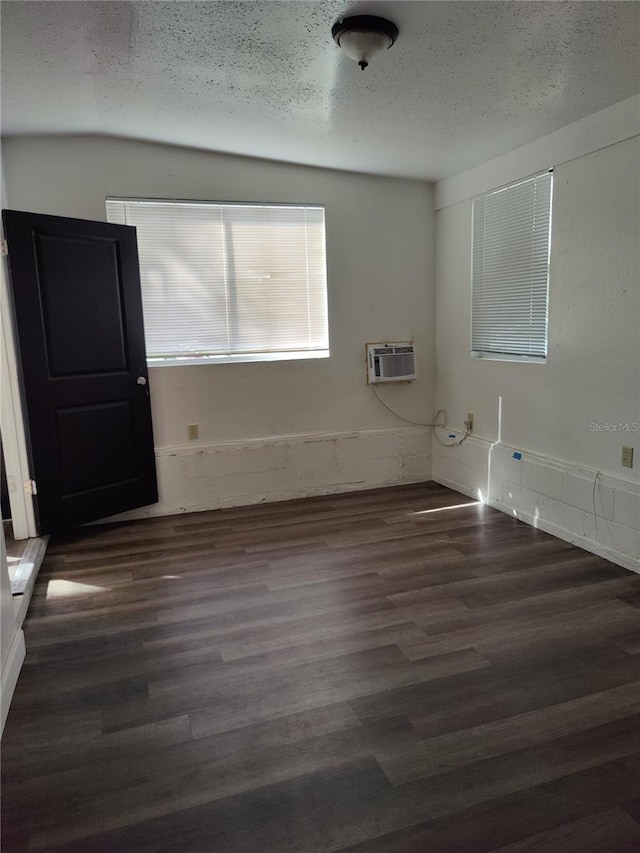 unfurnished room with a textured ceiling, dark wood-type flooring, and a wall mounted AC